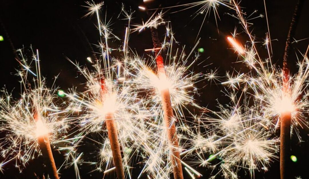 Several sparklers all shine together as their sparks light up the darkness.