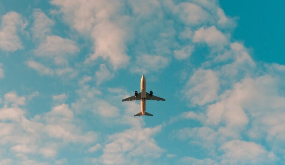 A lone plane flies through a cloudy, blue sky.