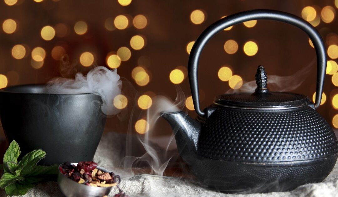 An ancient-looking copper kettle sits next to a cup of smoking liquid.