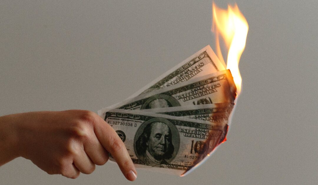 A hand holds out several hundred dollar bills as they burn.