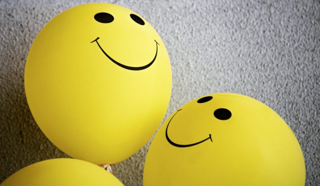 Two bright yellow balloons with happy faces on them smile at each other.