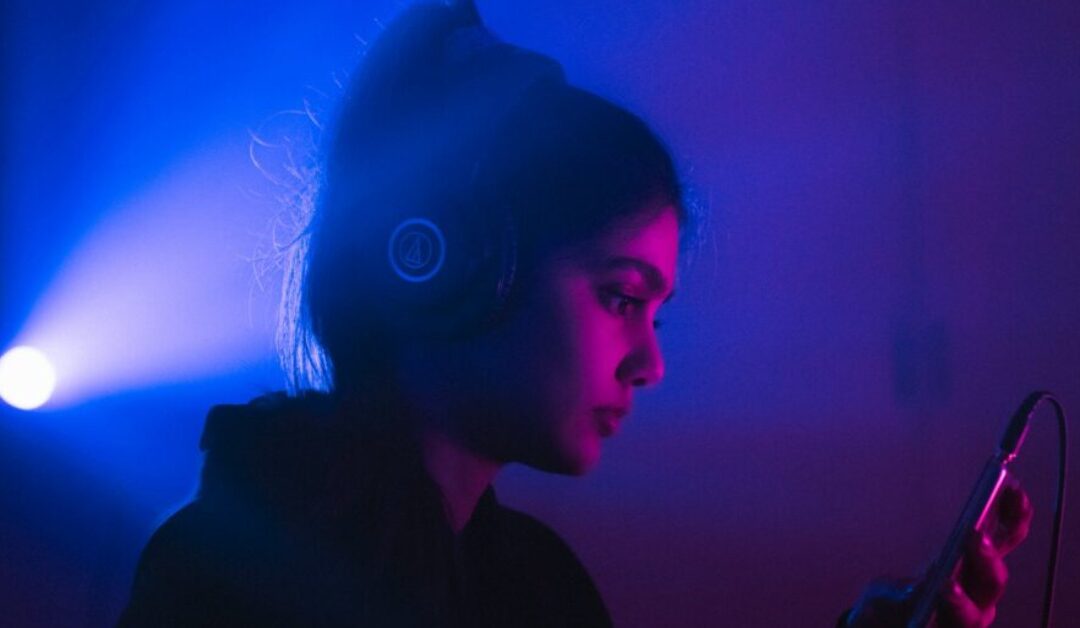 Blue and purple lights shine behind a girl with headphones on as she chooses a song to play.