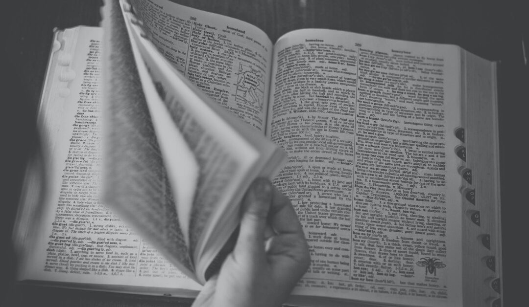 A black and white photo shows a hand fanning through the pages of a large dictionary.