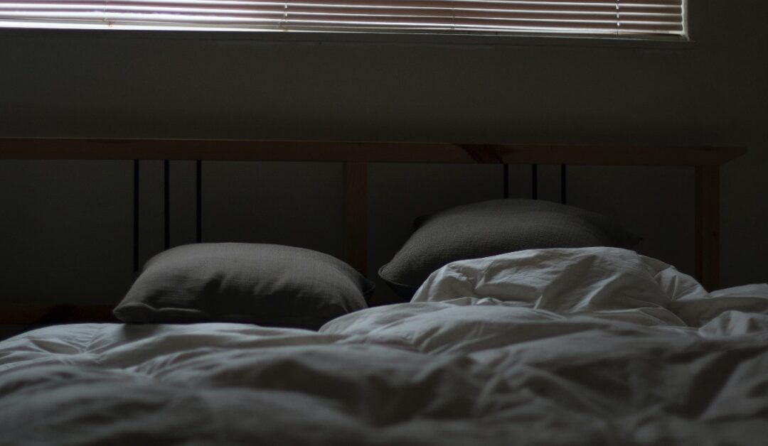 Messy pillows and sheets on a bed are shown in a dimly lit room.