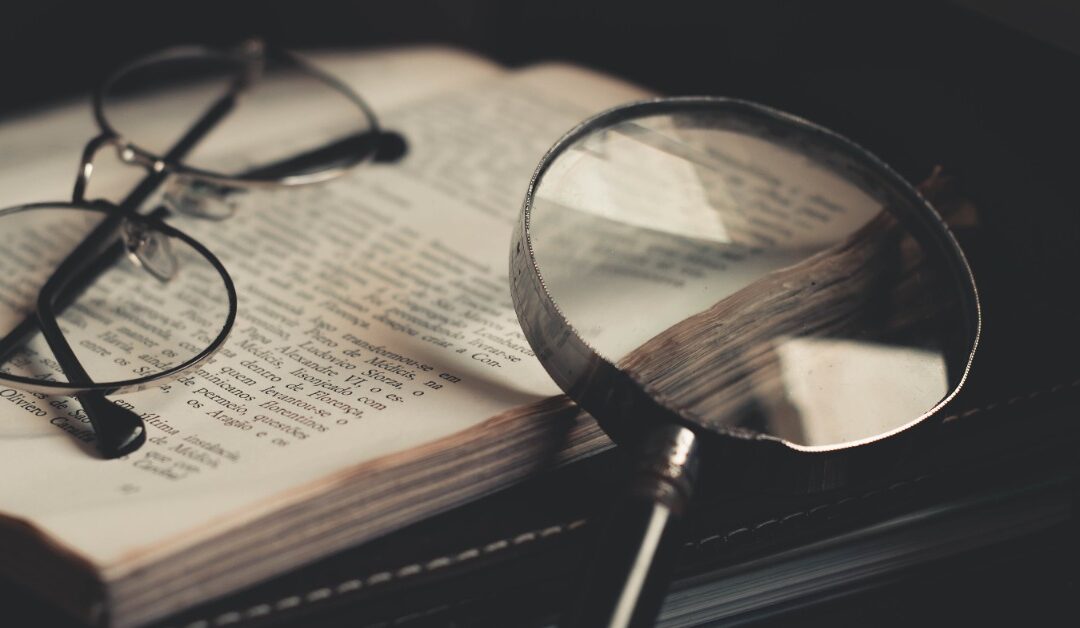 A magnifying glass sits on a book next to a pair of glasses.